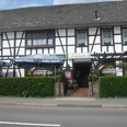 Lehmbacher Hof Fachwerkhaus mit Restaurant. Vor dem Gebäude stehen Biergarten-Sonnenschirme und grüne Hecke.