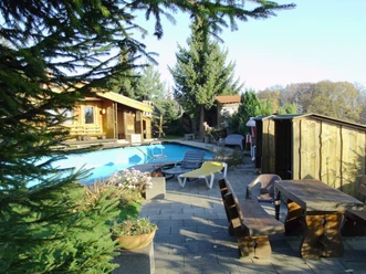 Eifgen-Sauna Ein Holzhaus mit Terrasse und Pool im Garten, umgeben von Bäumen und Sonnenliegen, idyllische Atmosphäre.