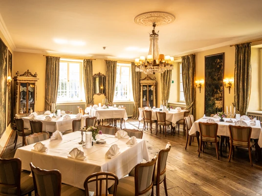 Schloss Auel Eleganter Speisesaal mit gedeckten Tischen, antiken Möbeln und einem Kronleuchter in warmem Licht.