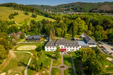 Schloss Auel <p>Luftaufnahme eines großen weißen Herrenhauses umgeben von grünen Wiesen und Wäldern in hügeliger Landschaft.</p>