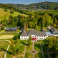 Schloss Auel <p>Luftaufnahme eines großen weißen Herrenhauses umgeben von grünen Wiesen und Wäldern in hügeliger Landschaft.</p>