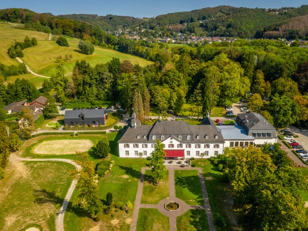 Schloss Auel <p>Luftaufnahme eines großen weißen Herrenhauses umgeben von grünen Wiesen und Wäldern in hügeliger Landschaft.</p>