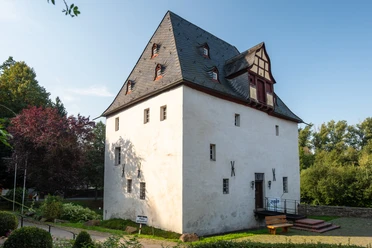 Golfplatz Burg Overbach <p>Historisches Fachwerkhaus im Sonnenschein, umgeben von grüner Vegetation und blühenden Bäumen.</p>