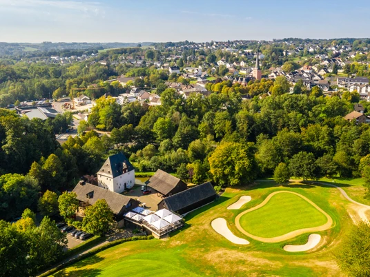 Golfplatz Burg Overbach <p>Luftaufnahme eines grünen Golfplatzes bei Much, umgeben von dichter Waldlandschaft und Gebäuden.</p>