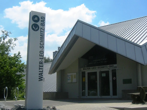 Eingangsbereich Das Walter-Leo-Schmitz-Bad mit modernem Gebäude und Schild bei sonnigem Himmel.