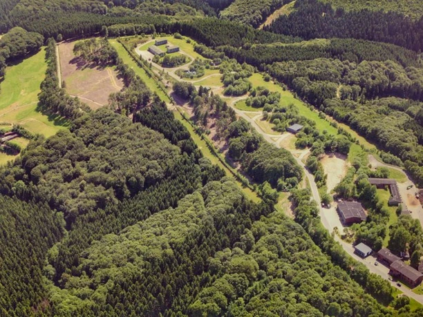 image Luftaufnahme eines weitläufigen Waldgebiets mit mehreren Gebäuden und Straßen, umgeben von grünen Bäumen.