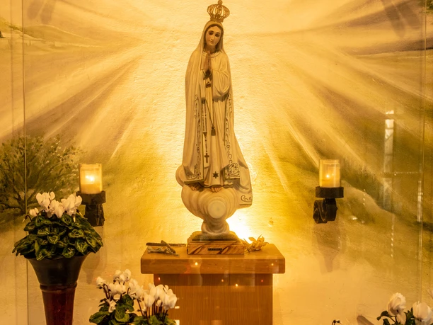 image Madonna-Statue in Strahlenlicht, umgeben von Blumenarrangements. Feierlich und spirituell.