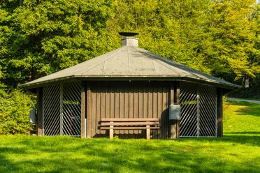 Fatimakapelle Ein hölzerner Pavillon vor saftigem Grün mit Bank im Vordergrund, ideal für eine Rast im Freien.