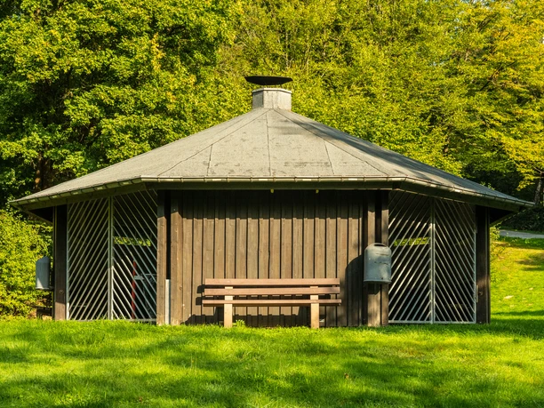 Fatimakapelle Ein hölzerner Pavillon vor saftigem Grün mit Bank im Vordergrund, ideal für eine Rast im Freien.