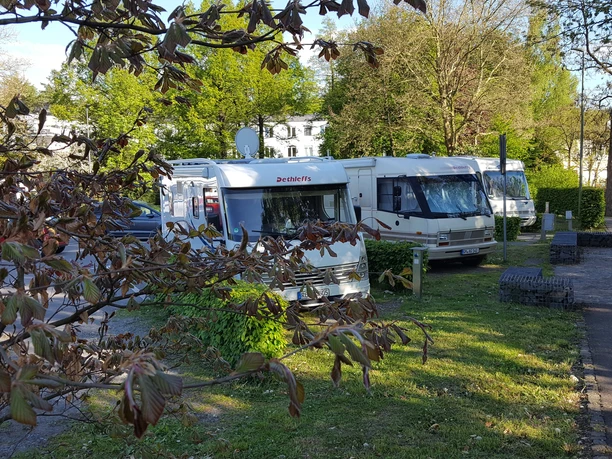 Wohnmobile auf dem Stellplatz Ohler Wiesen Drei Wohnmobile parken nebeneinander auf einem begrünten Stellplatz, umgeben von Bäumen und Hecken.