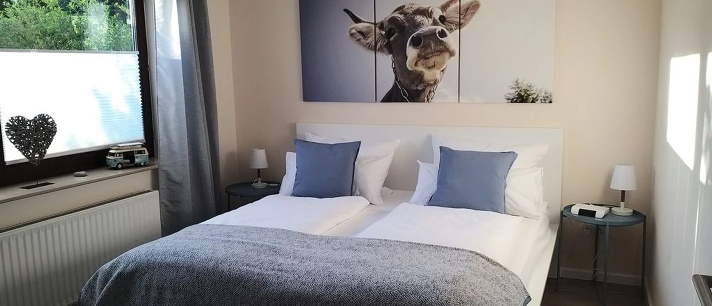 Schlafzimmer 1 Gemütliches Schlafzimmer mit Doppelbett, blau-weißer Bettwäsche, Kuhbild über dem Bett, Tageslicht.