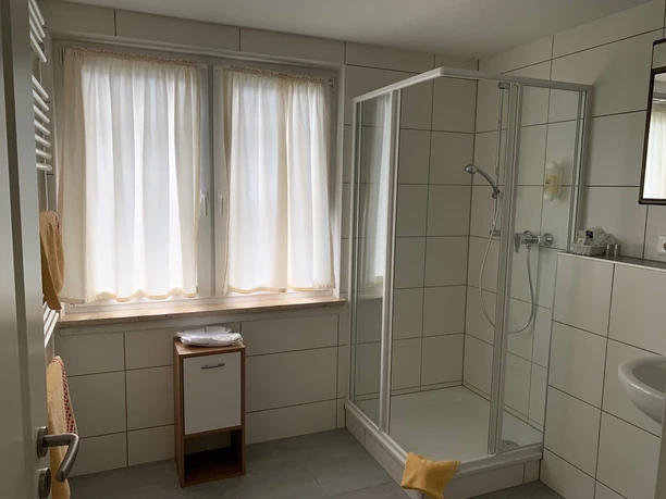 image Helles, modern gefliestes Badezimmer mit Dusche, Fenster, Heizkörper und kleinem Waschtisch.
