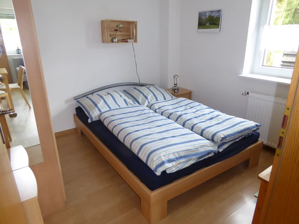 Ferienwohnung im Bergischen Land Helles Schlafzimmer mit einem Doppelbett, gestreiften Bettdecken, einem Fenster und Bildern an der Wand.