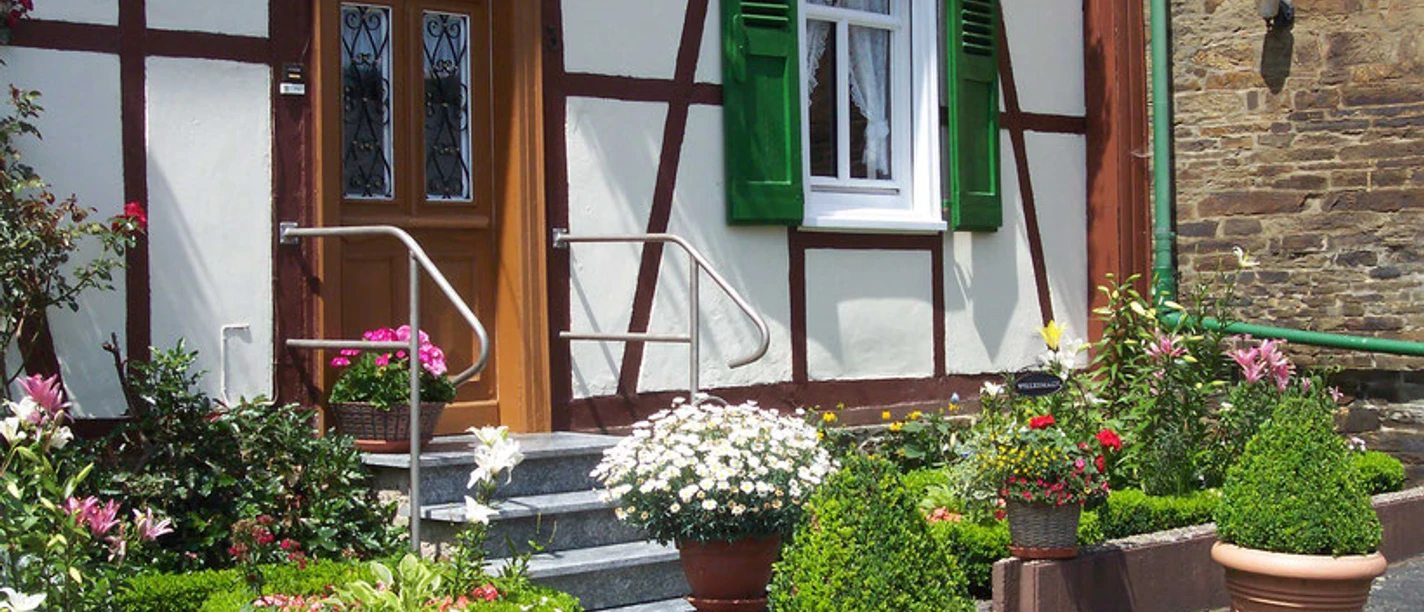 image Ein einladender Fachwerkhauseingang mit blühendem Vorgarten und begrünten Terrakottagefäßen.