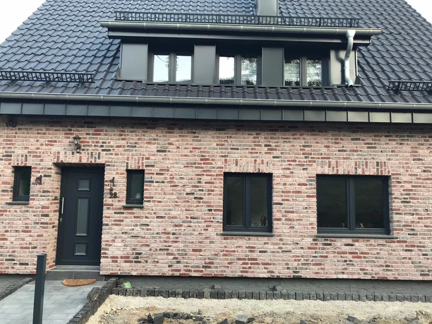 Außenansicht Ein modernes Backsteinhaus mit dunkelgrauem Dach, großen Fenstern und weißem Eingang in ruhiger Umgebung.