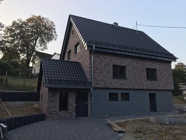 Außenansicht Neubau eines zweistöckigen Einfamilienhauses aus Ziegelstein mit dunkelgrauem Dach in ländlicher Umgebung.