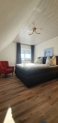 Schlafzimmer Gemütliches Schlafzimmer mit Doppelbett, Parkettboden, rotem Sessel, hellem Holzpaneel an der Decke.
