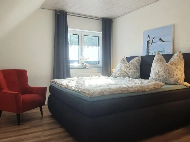 Schlafzimmer Gemütliches Schlafzimmer mit Doppelbett, Parkettboden, rotem Sessel, hellem Holzpaneel an der Decke.