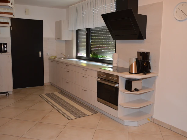 Küche Moderne Einbauküche mit Herd, Dunstabzugshaube, Kaffeemaschine und Fenster, helle Fliesenböden.