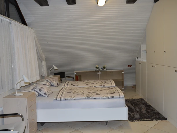 Schlafzimmer Schlafzimmer mit Doppelbett, schräge weiße Decke, seitlichen Schränken und Nachttischen mit Lampen.