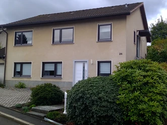 Außenansicht Zweistöckiges, beiges Einfamilienhaus mit Satteldach, weißen Fensterrahmen und grünem Vorgarten.