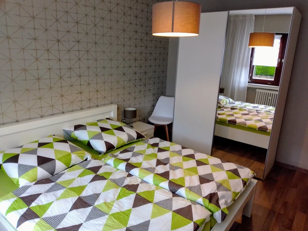 Schlafzimmer Modernes Schlafzimmer mit Doppelbett, geometrischer Bettwäsche, Spiegelschrank und hölzernem Boden.