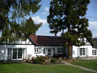 image Ein weißes Landhaus mit braunem Ziegeldach, umgeben von hohen Bäumen und Grünflächen.