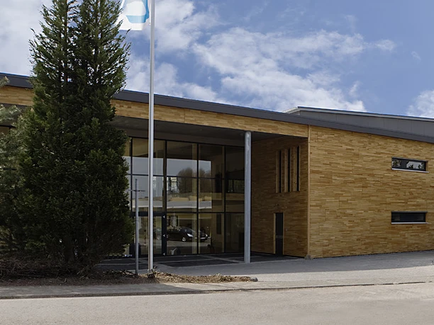 Außenaufnahme Ein modernes Gebäude mit großen Glasfenstern, umgeben von Bäumen, unter einem strahlend blauen Himmel.