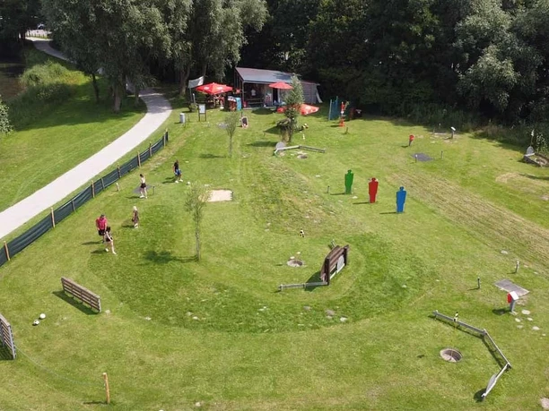 Activity Park FussBallGolf - Die Anlage Grüne Fußballgolf-Anlage mit bunten Hindernissen und Spielern im Sonnenschein.