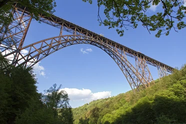 Müngstener Brücke Hoch über bewaldetem Tal überspannt die Müngstener Brücke zwischen Bäumen den blauen Himmel.