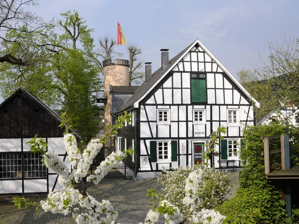 Heimatmuseum Bergneustadt Fachwerkhaus mit deutschem Schieferdach, blühende Bäume im Vordergrund, Flagge auf Turm hinten.