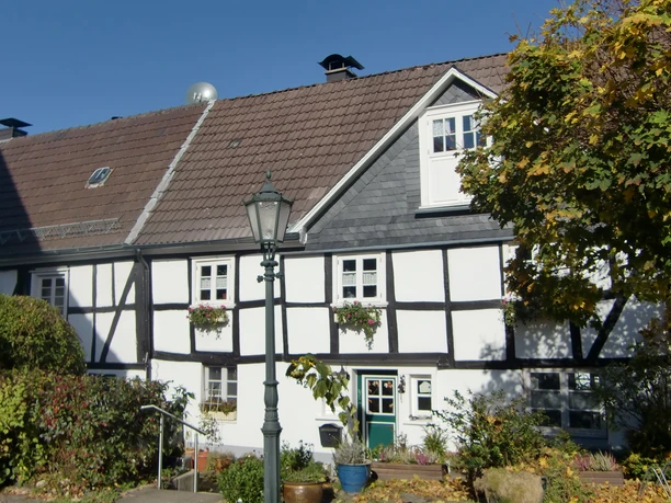 In der Altstadt Bergneustadt Fachwerkhaus mit weißer Fassade und schwarzen Balken, umgeben von Herbstbäumen und Laterne.