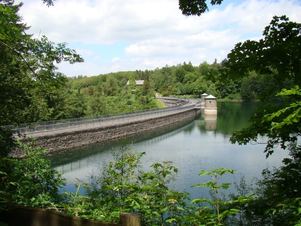 Neye-Talsperre Talsperre in grüner Umgebung mit Wald und Gewässer, im Hintergrund ein Turm auf der Mauer.