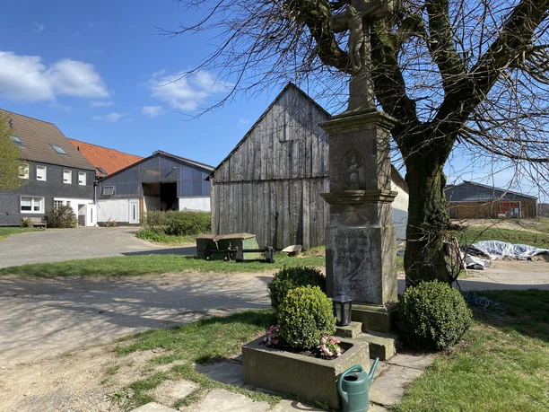 Wegekreuz in Lendinghausen <p>Ein alter steinerner Wegweiser steht vor einem Bauernhof neben einem Baum unter blauem Himmel.</p>