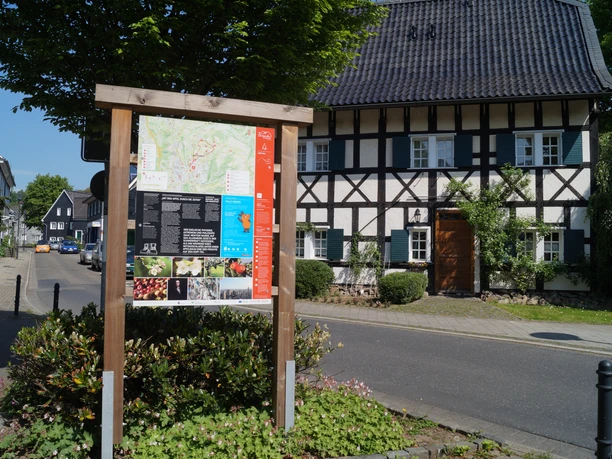 Infotafel am Obstweg Ein traditionelles Fachwerkhaus hinter einem Infoboard an einer sonnigen Straße in Leichlingen.