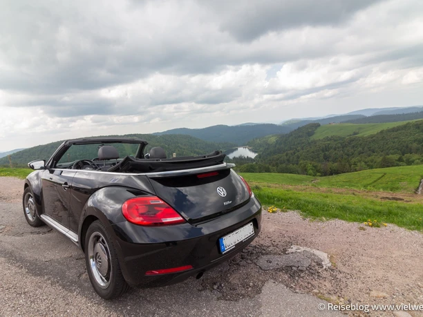 Talsperren-Route Ein schwarzer VW Cabrio parkt auf einer Straße mit Blick auf eine grüne Hügellandschaft.