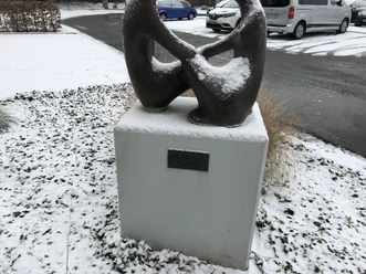 Skulptur "Das Gespräch", bedeckt mit Schnee, steht auf einem Sockel in verschneiter Umgebung.