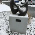 Skulptur "Das Gespräch", bedeckt mit Schnee, steht auf einem Sockel in verschneiter Umgebung.