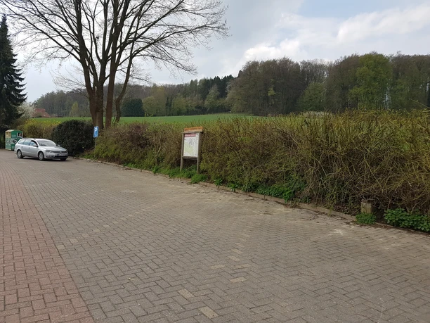 Wanderparkplatz mit Autos, umgeben von Bäumen und Feldern, der als Startpunkt für Naturwanderungen dient.