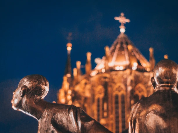 Bronze-Figuren bei Dunkelheit mit dem beleuchteten Aachener Dom im Hintergrund.