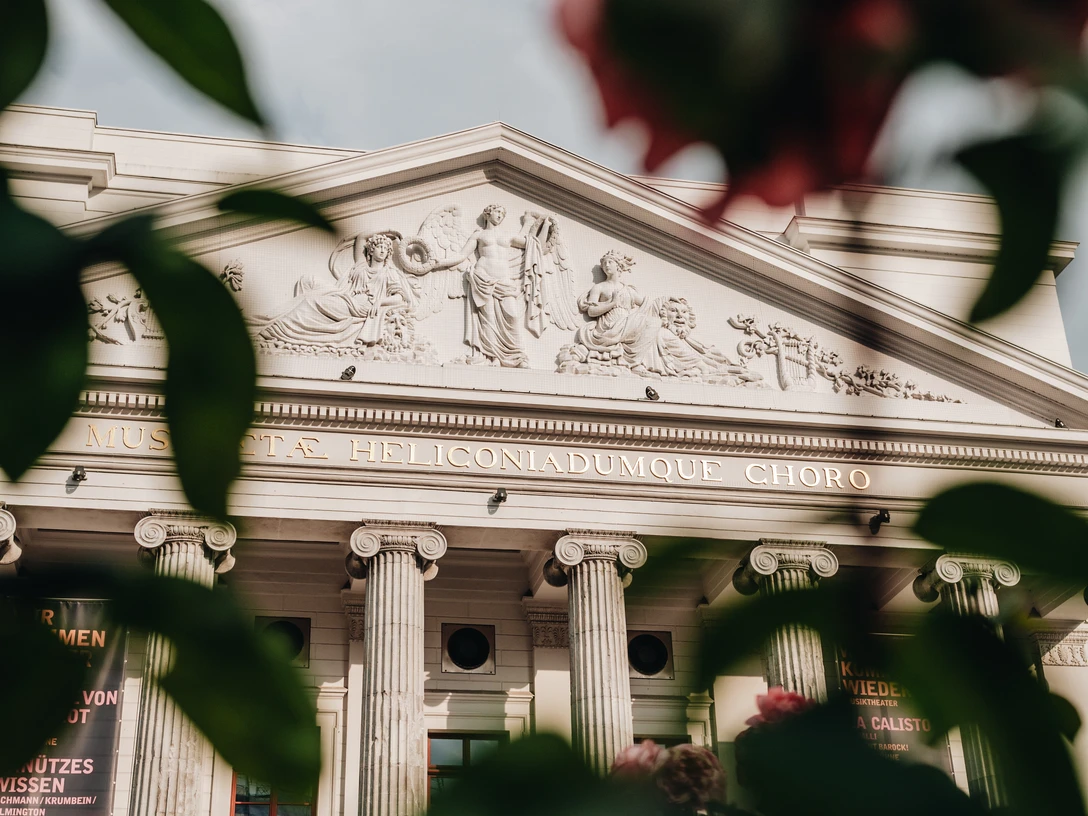 Blick auf die Vorderseite des Theaters Aachen durch Blätter hindurch.