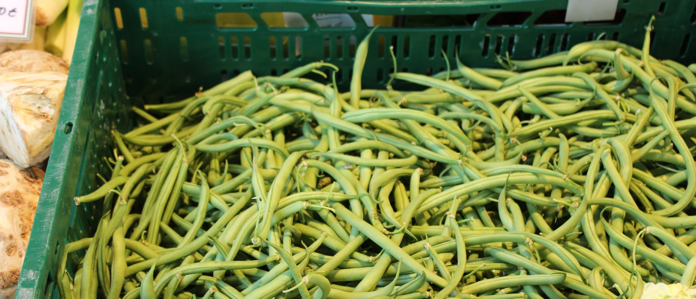 Verse sperziebonen in een groene plastic krat op een wekelijkse markt, omringd door groenten.