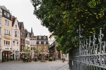 Münsterplatz Aachen Kleine, ruhiger Platz mit Geschäften und Außengastronomie und zwei Bäumen.