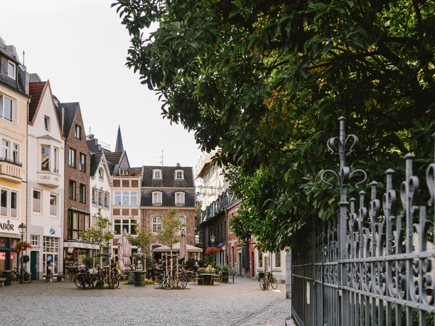 Münsterplatz Aachen Kleine, ruhiger Platz mit Geschäften und Außengastronomie und zwei Bäumen.