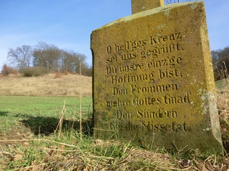 Wegekreuze sind ein typisches Merkmal für das Kulturland Kreis Höxter Steinernes Wegekreuz mit eingraviertem Gebet steht in ländlicher Umgebung vor einem Hügel.