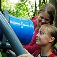 Kinder betrachten neugierig ein blaues Kaleidoskop auf einer Metallhalterung im Grünen des Rosenbergs.