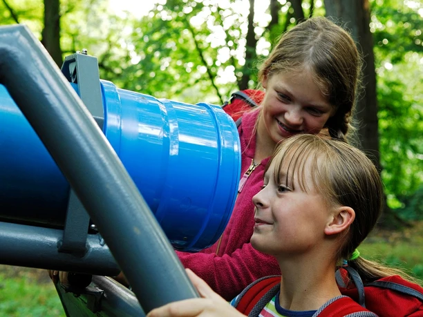 Bad Driburg-Kaleidoskopweg-Wippenkaleidoskop auf dem Rosenberg Kinder betrachten neugierig ein blaues Kaleidoskop auf einer Metallhalterung im Grünen des Rosenbergs.