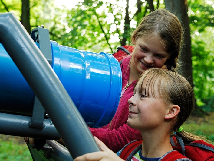 Bad Driburg-Kaleidoskopweg-Wippenkaleidoskop auf dem Rosenberg Kinder betrachten neugierig ein blaues Kaleidoskop auf einer Metallhalterung im Grünen des Rosenbergs.