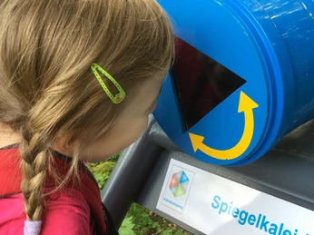 Hineinschauen und Funfoto machen Ein Kind schaut in ein blaues Spiegelscope, das ein kaleidoskopisches Erlebnis bietet.