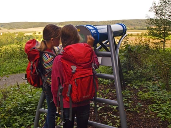 Mädchen mit Rucksäcken schauen durch das Sphäriskop Zwei Mädchen mit roten Rucksäcken betrachten die Landschaft durch ein Sphäriskop in einer grünen Umgebung.